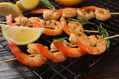 Photo of Skewers with delicious grilled shrimps, herbs and lemon on wooden table, closeup