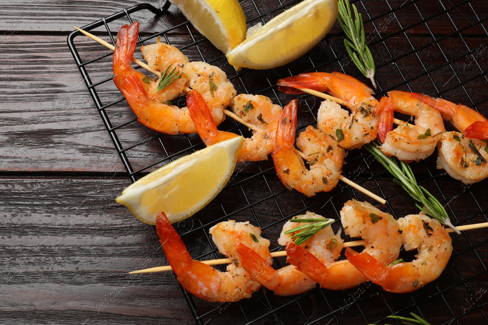 Photo of Skewers with delicious grilled shrimps, herbs and lemon on wooden table, flat lay