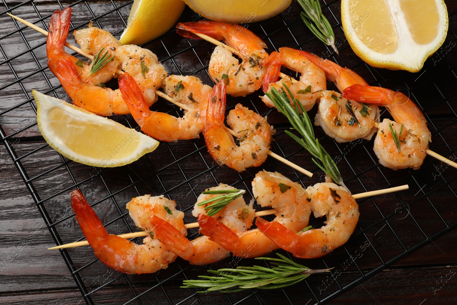 Photo of Skewers with delicious grilled shrimps, herbs and lemon on wooden table, flat lay