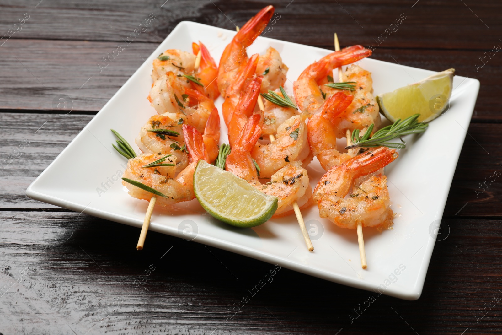 Photo of Skewers with delicious grilled shrimps and lime on wooden table