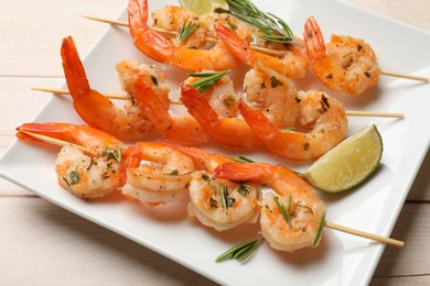 Photo of Skewers with delicious grilled shrimps and lime on wooden table, closeup