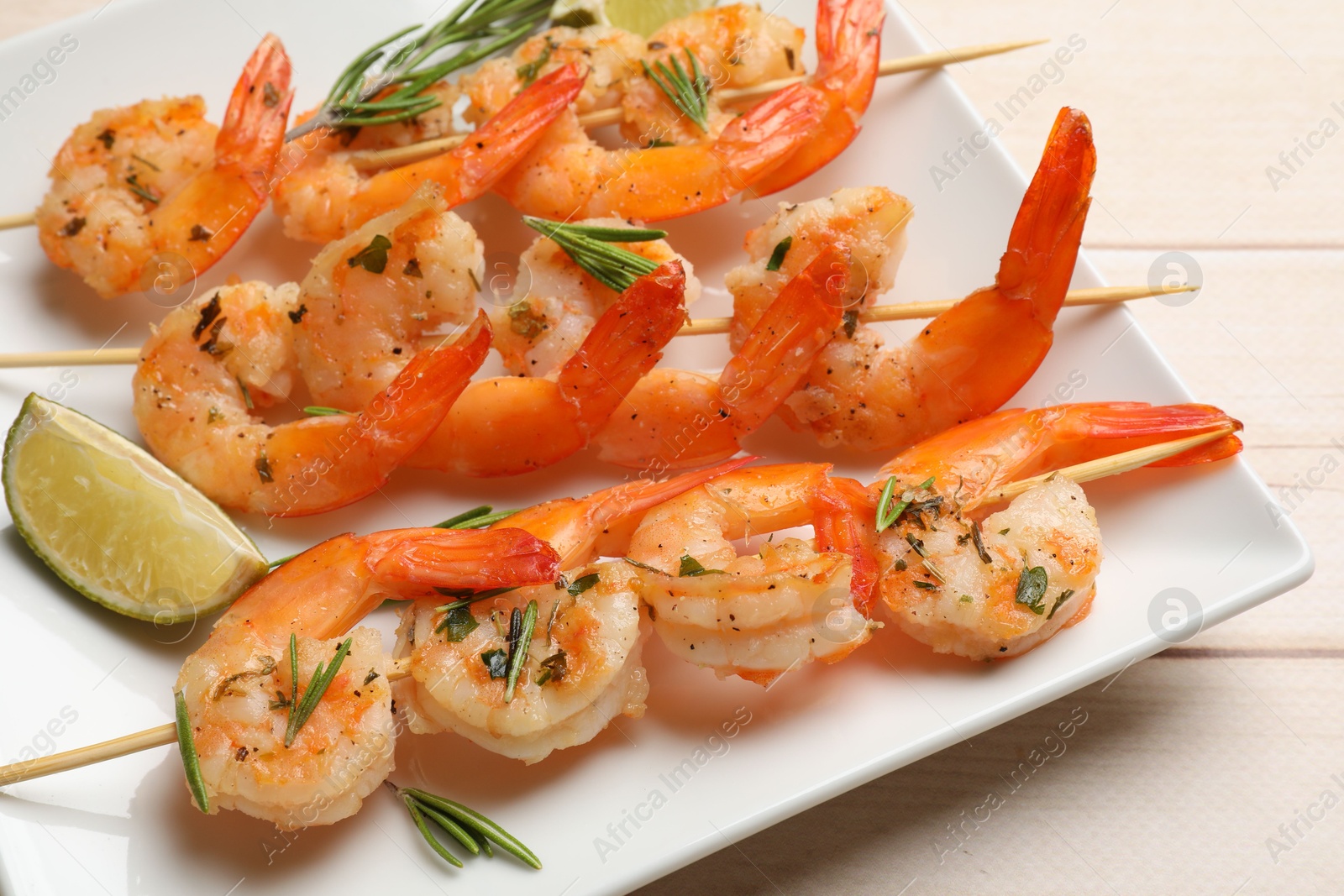 Photo of Skewers with delicious grilled shrimps and lime on wooden table, closeup