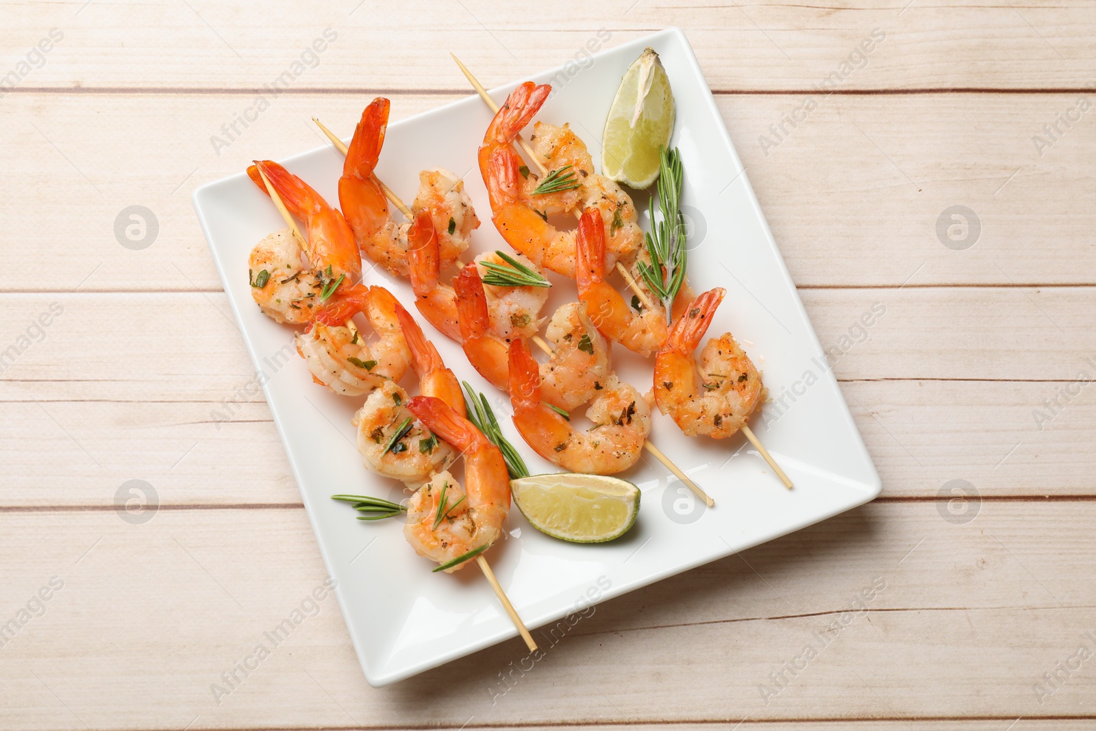 Photo of Skewers with delicious grilled shrimps and lime on wooden table, top view