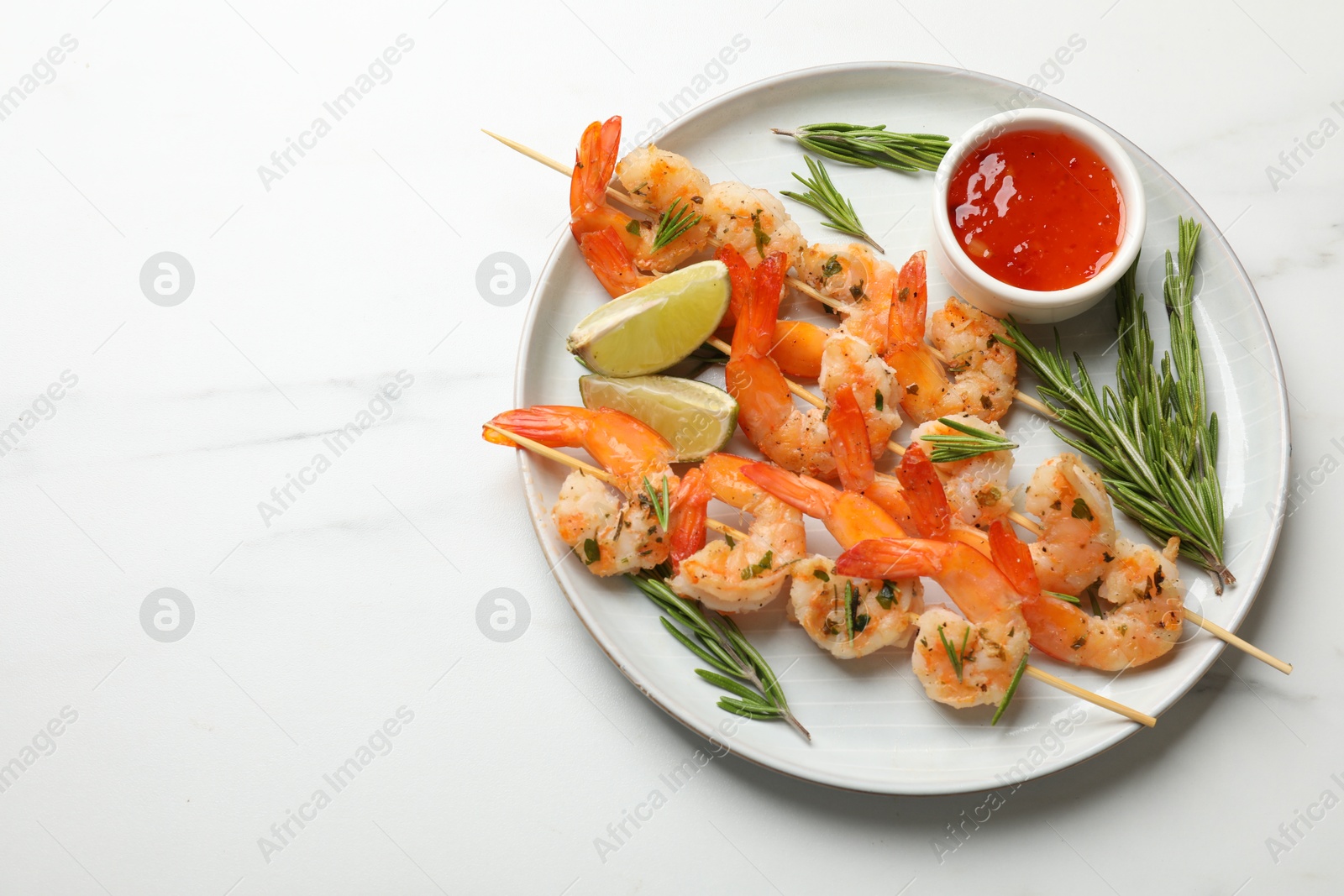 Photo of Skewers with delicious grilled shrimps served on white marble table, top view. Space for text