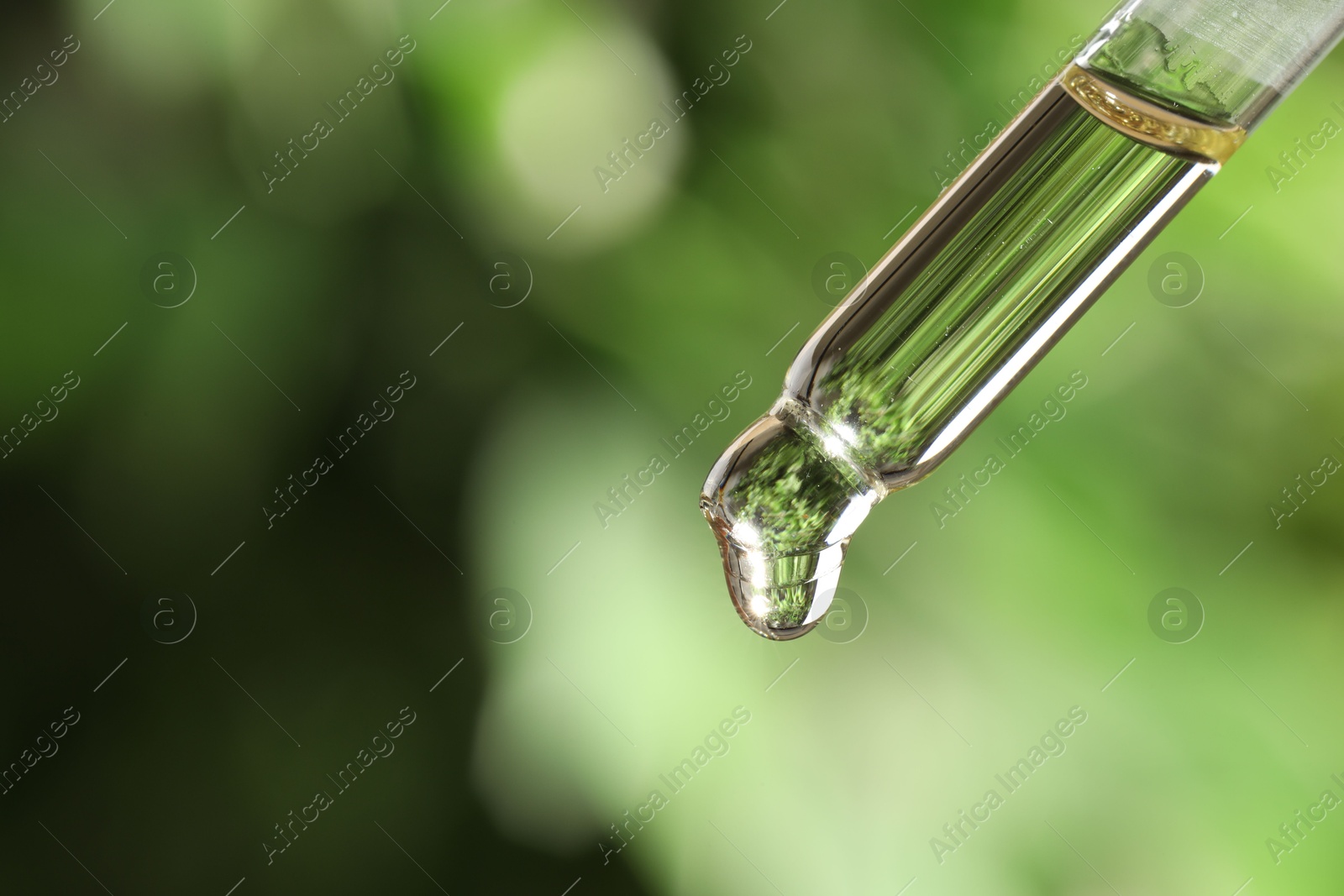 Photo of Essential oil dripping from pipette against blurred green background, closeup. Space for text