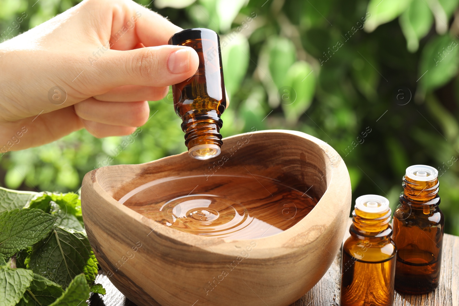 Photo of Woman dripping essential oil into wooden bowl of water on table, closeup