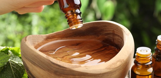 Woman dripping essential oil into bowl of water against blurred green background, closeup. Banner design