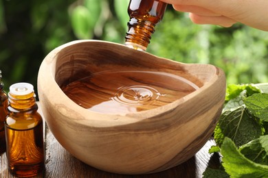 Woman dripping essential oil into wooden bowl of water on table, closeup