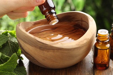 Woman dripping essential oil into wooden bowl of water on table, closeup