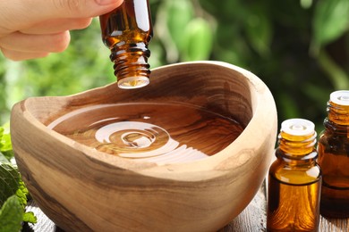 Photo of Woman dripping essential oil into wooden bowl of water on table, closeup