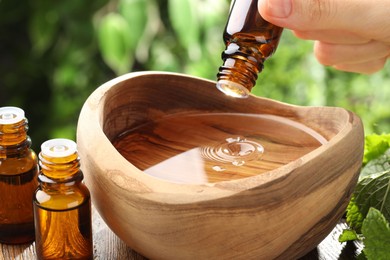 Photo of Woman dripping essential oil into wooden bowl of water on table, closeup