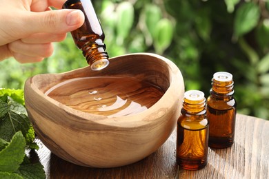 Photo of Woman dripping essential oil into wooden bowl of water on table, closeup