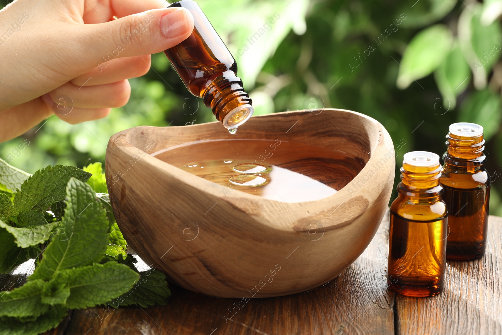 Photo of Woman dripping essential oil into wooden bowl of water on table, closeup