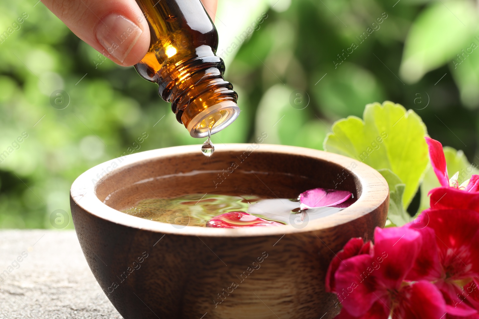 Photo of Woman dripping essential oil into wooden bowl of water on table, closeup