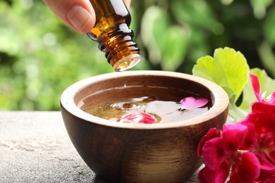 Photo of Woman dripping essential oil into wooden bowl of water on table, closeup