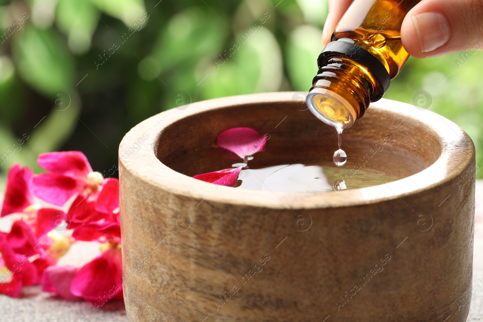 Photo of Woman dripping essential oil into wooden bowl of water on table, closeup