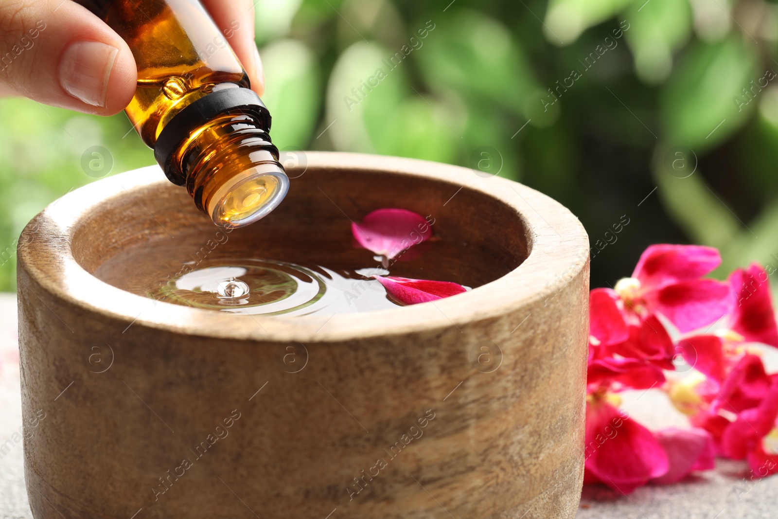 Photo of Woman dripping essential oil into wooden bowl of water on table, closeup