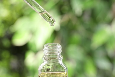 Essential oil dripping from pipette into bottle against blurred green background, closeup