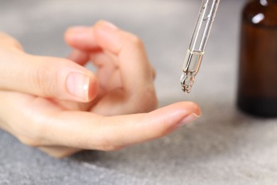 Photo of Woman dripping essential oil onto finger at grey table, closeup