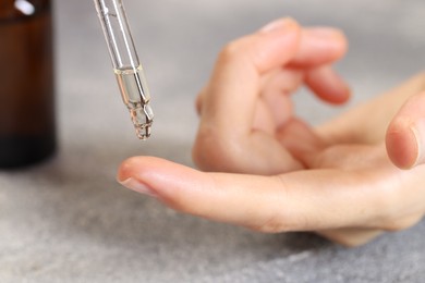 Photo of Woman dripping essential oil onto finger at grey table, closeup