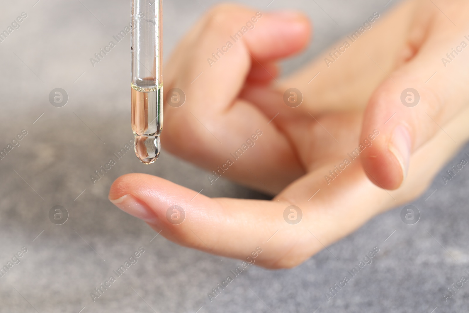 Photo of Woman dripping essential oil onto finger at grey table, closeup