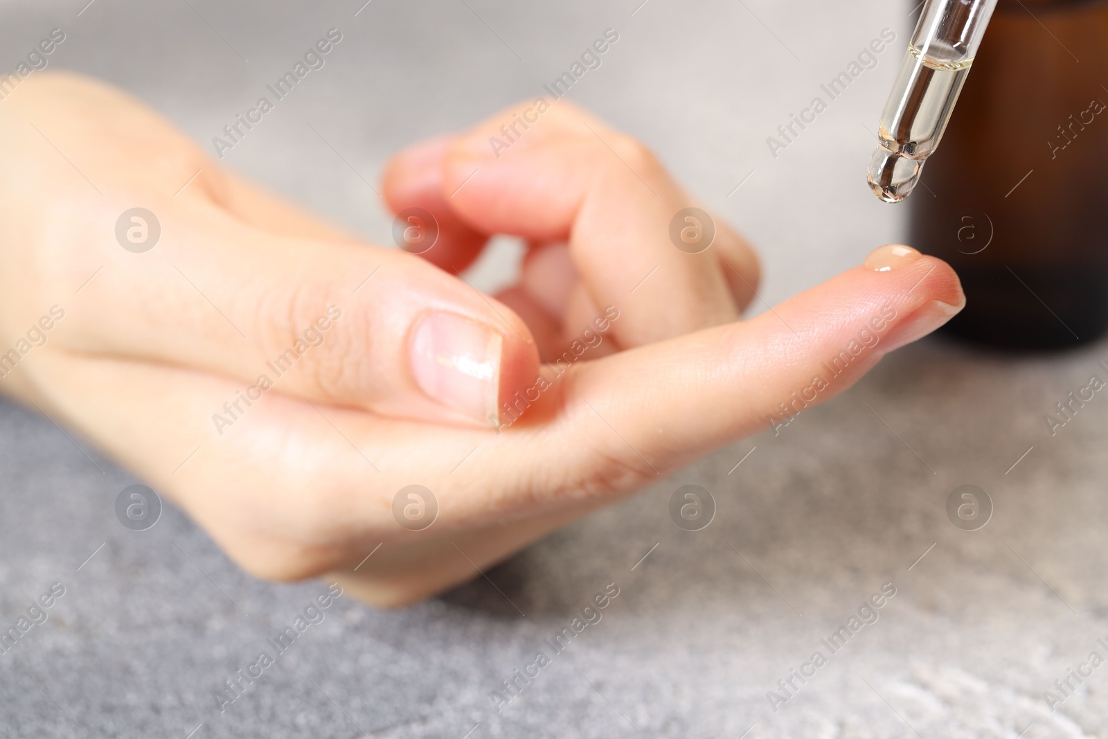 Photo of Woman dripping essential oil onto finger at grey table, closeup