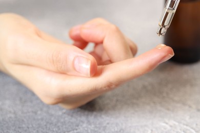 Woman dripping essential oil onto finger at grey table, closeup