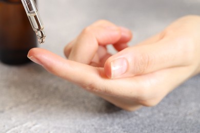 Photo of Woman dripping essential oil onto finger at grey table, closeup