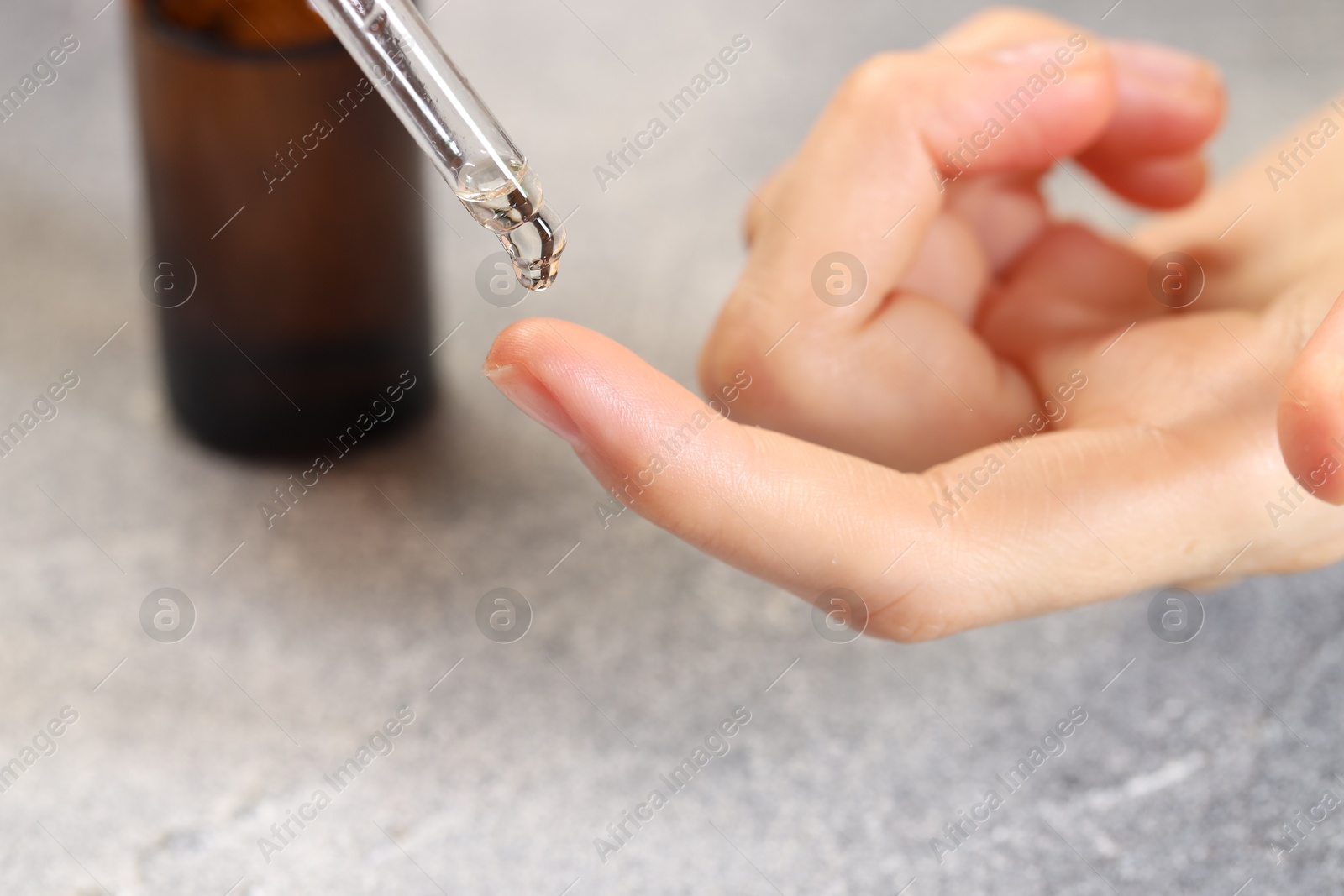 Photo of Woman dripping essential oil onto finger at grey table, closeup