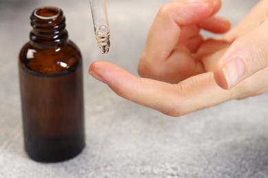 Photo of Woman dripping essential oil onto finger at grey table, closeup