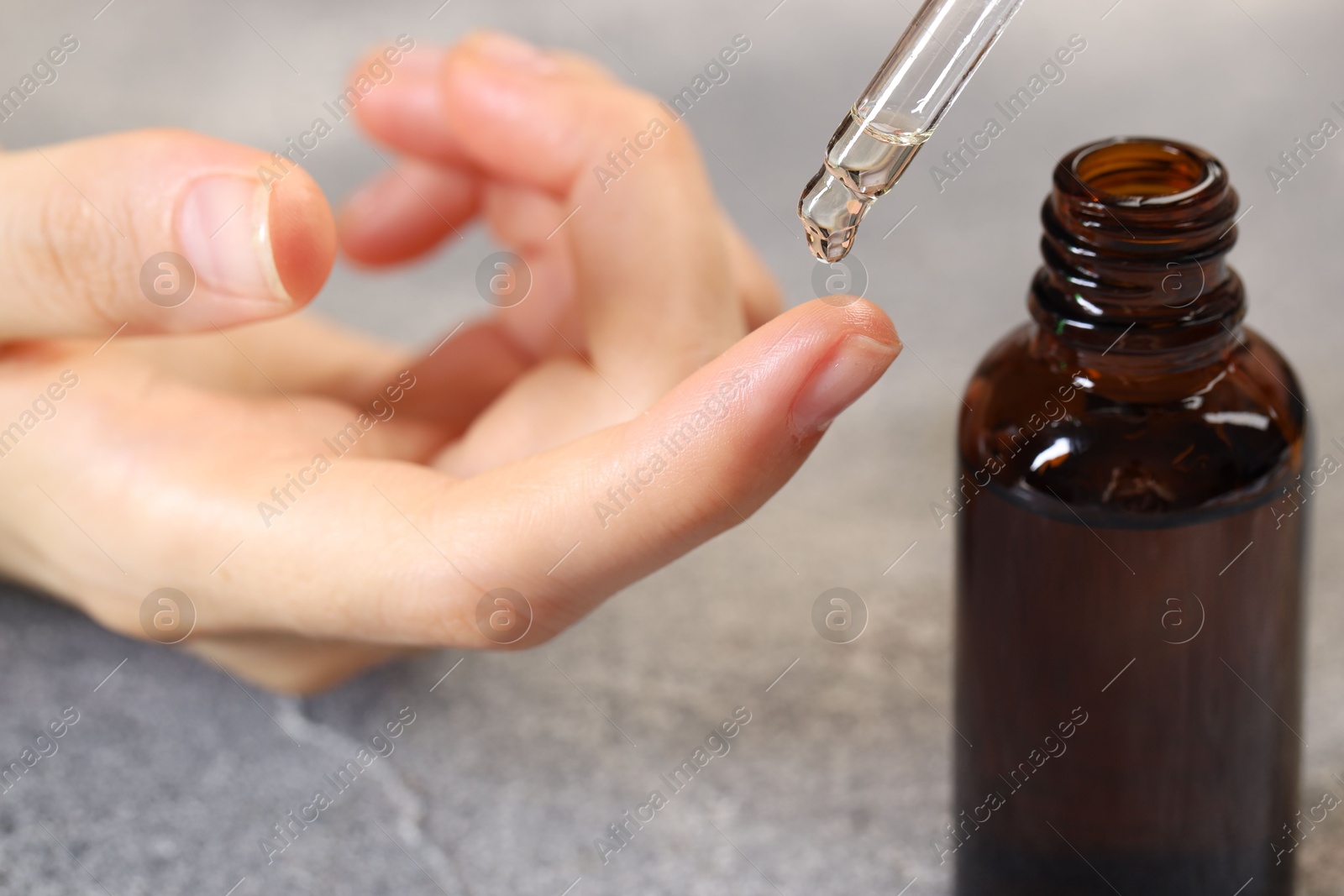 Photo of Woman dripping essential oil onto finger at grey table, closeup