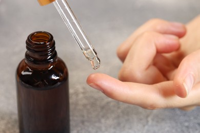 Photo of Woman dripping essential oil onto finger at grey table, closeup