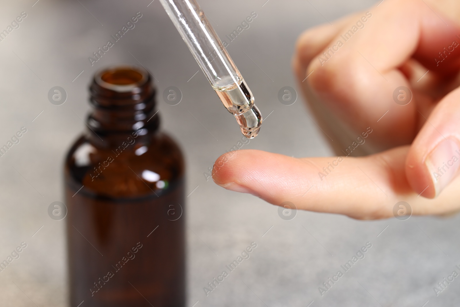 Photo of Woman dripping essential oil onto finger at grey table, closeup