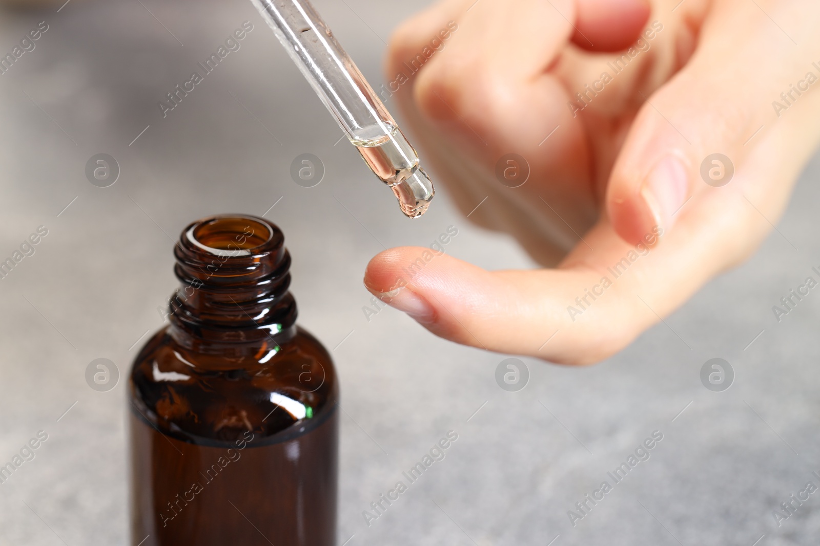 Photo of Woman dripping essential oil onto finger at grey table, closeup