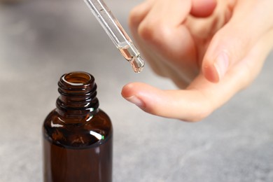 Photo of Woman dripping essential oil onto finger at grey table, closeup