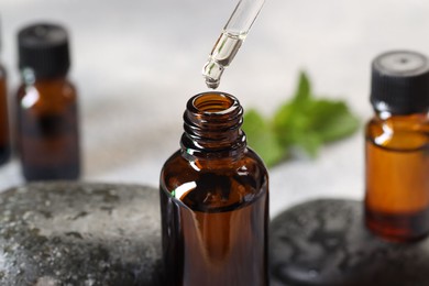 Photo of Essential oil dripping from pipette into bottle on table, closeup