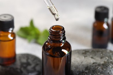 Photo of Essential oil dripping from pipette into bottle on table, closeup