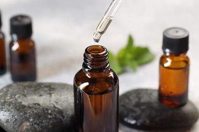 Photo of Essential oil dripping from pipette into bottle on table, closeup