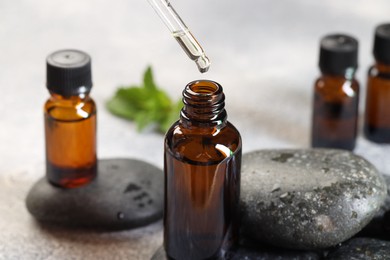 Photo of Essential oil dripping from pipette into bottle on table, closeup