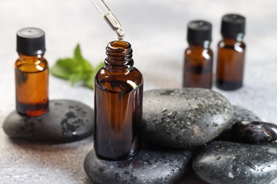 Photo of Essential oil dripping from pipette into bottle on table, closeup