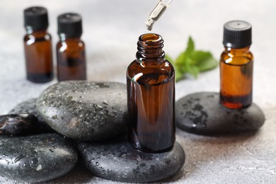 Photo of Essential oil dripping from pipette into bottle on table, closeup