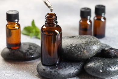 Photo of Essential oil dripping from pipette into bottle on table, closeup