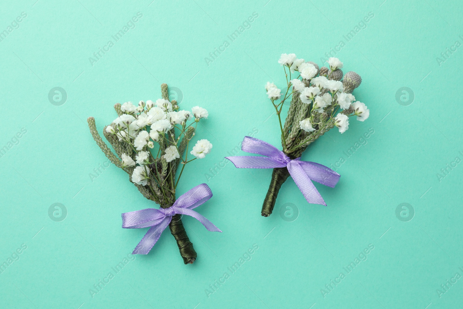 Photo of Small stylish boutonnieres on turquoise background, flat lay