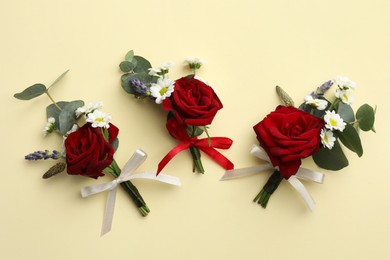 Many stylish red boutonnieres on beige background, flat lay