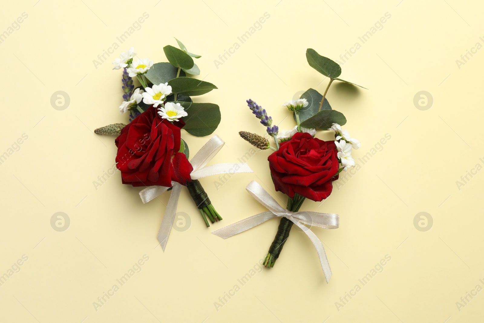 Photo of Stylish red boutonnieres on beige background, flat lay