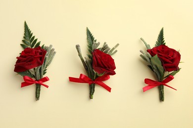 Many stylish red boutonnieres on beige background, flat lay