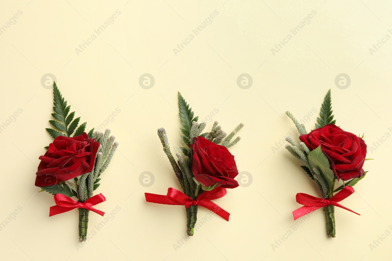 Photo of Many stylish red boutonnieres on beige background, flat lay