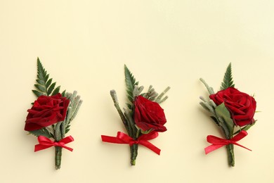 Many stylish red boutonnieres on beige background, flat lay