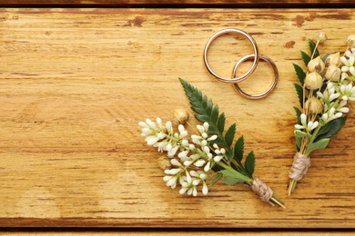 Photo of Small stylish boutonnieres and rings on wooden table, flat lay. Space for text