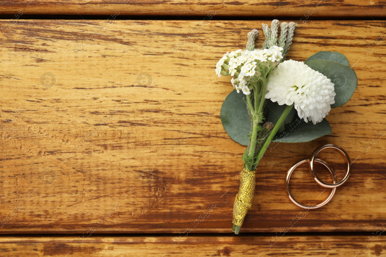 Photo of Small stylish boutonniere and rings on wooden table, flat lay. Space for text